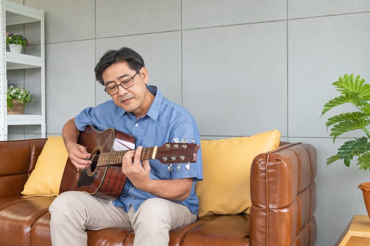 A senior man practices guitar in his living room.