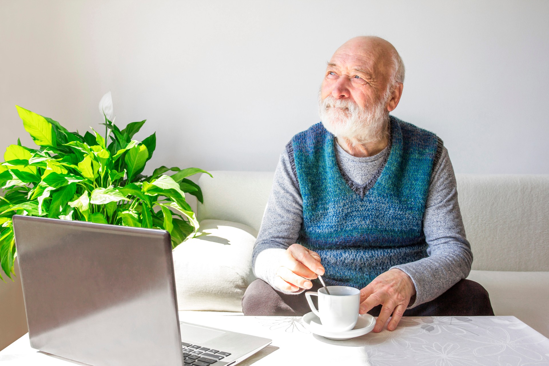 Senior man mixing his coffee while using his laptop