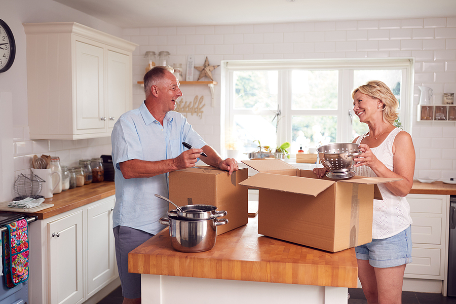 A senior couple smiles while unpacking moving boxes.