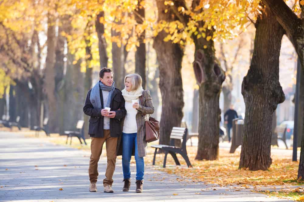 A senior couple walking through a city park during autumn