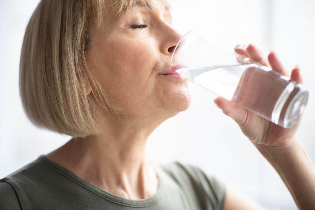 A senior woman staying hydrated by drinking a glass of water.