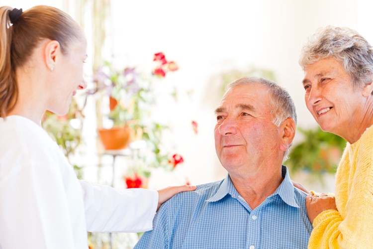 A smiling older couple talks with a caregiver.
