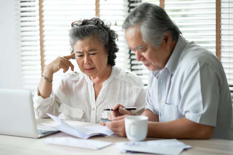 A senior couple looks at their retirement savings on a laptop.