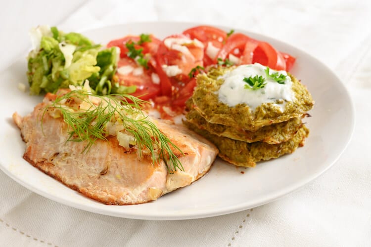 Salmon dinner served with vegetable pancakes and a tomato salad.
