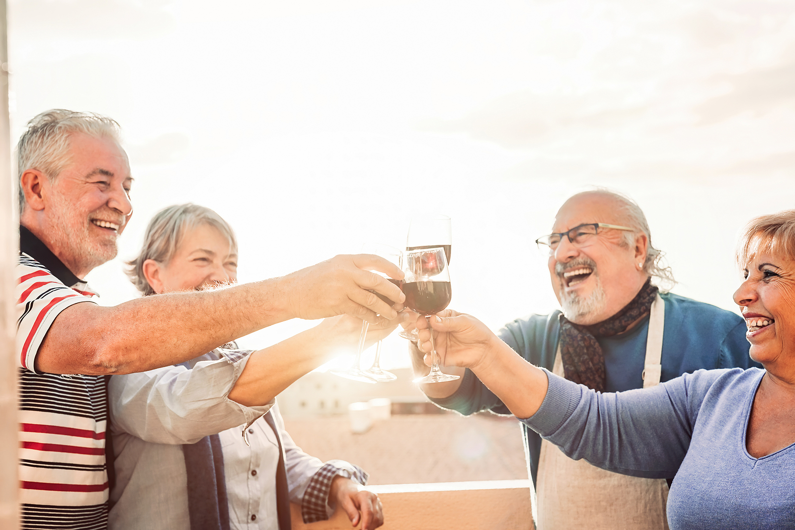 Senior friends clink glasses while enjoying wine outdoors together