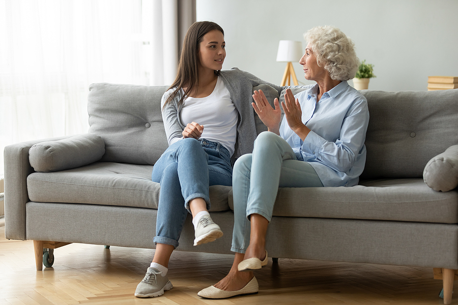 Adult daughter and older adult mother talking on the couch about the benefits of living in a senior community