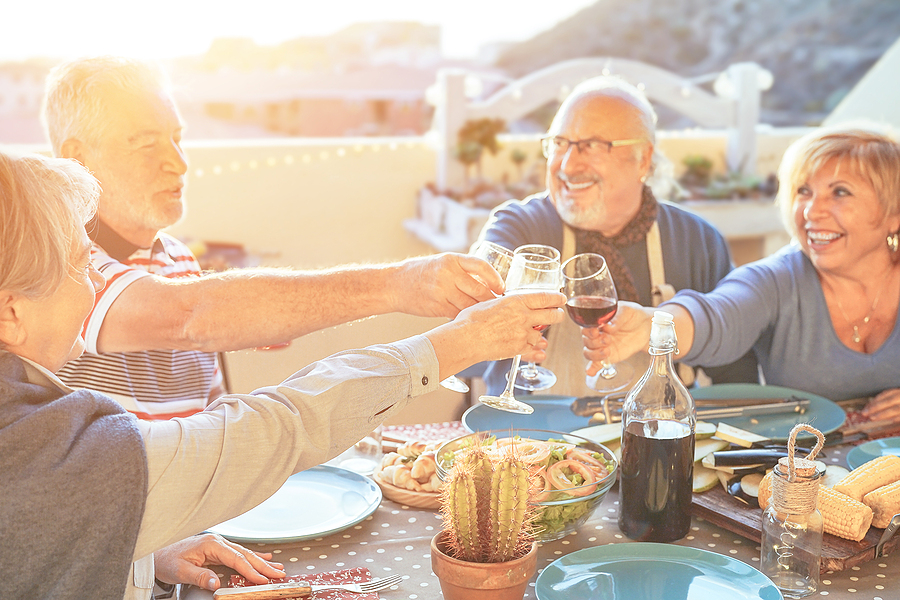 A group of older adults cheering with red wine at barbecue in terrace outdoor.