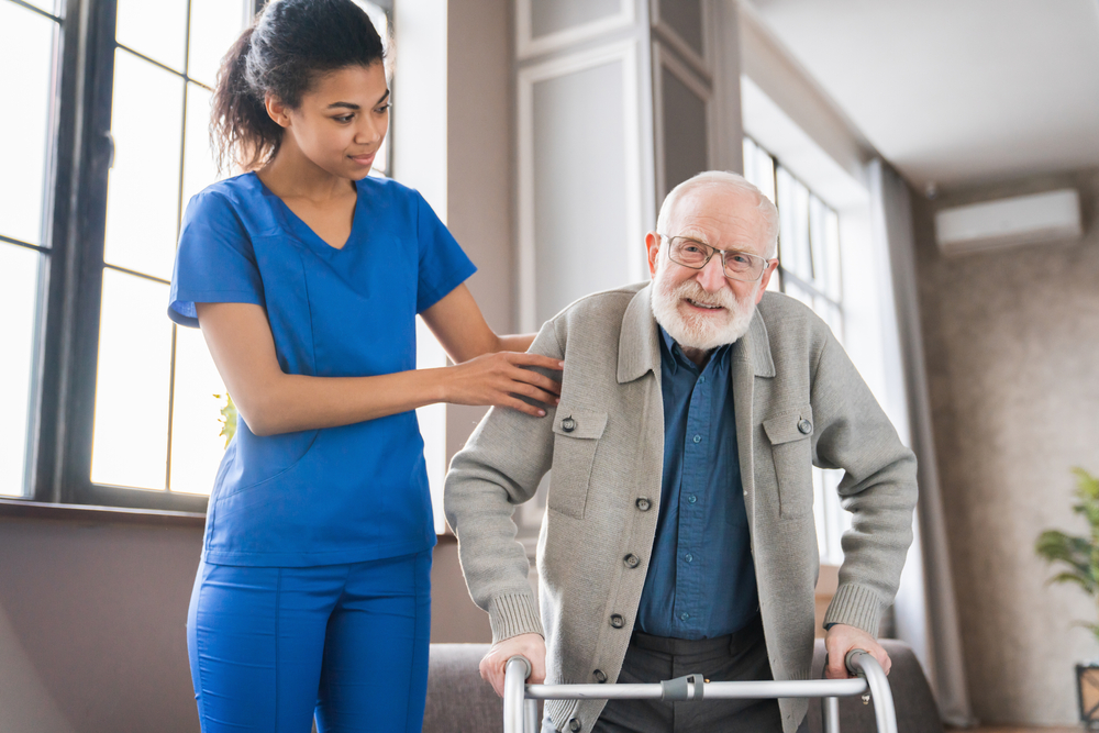 An occupational therapist helps a senior man use a walker to maintain mobility and independence