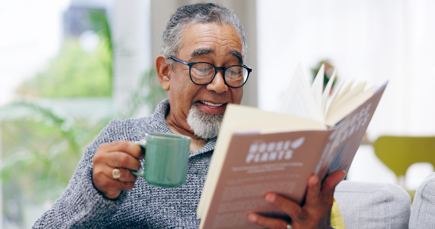 An older senior man drinking tea and doing summer reading